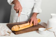 front-view-chef-wearing-white-clothes-cutting-baguette-min